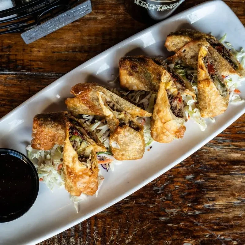 Plate of golden-brown fried food halves with filling, cabbage, and sauce.