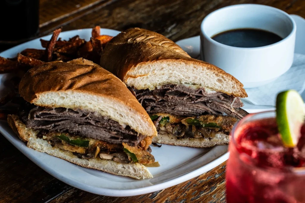 Close-up of a sliced beef and cheese sandwich with sweet potato fries.