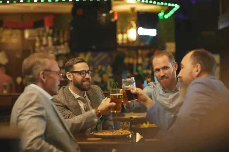 Four men toast with beers and snacks at a bar.