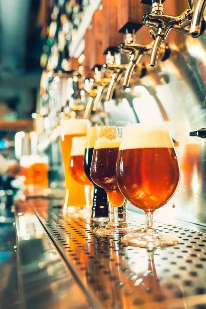 Three glasses of beer, light to dark, on a metal bar.