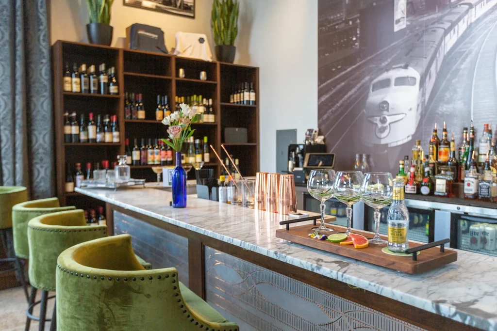 Marble bar counter, olive velvet stools, drinks, and train mural.