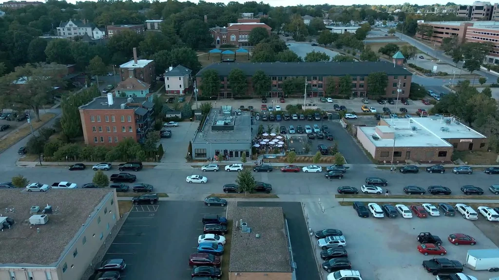 Aerial view: busy neighborhood, restaurant patio, many cars, trees.