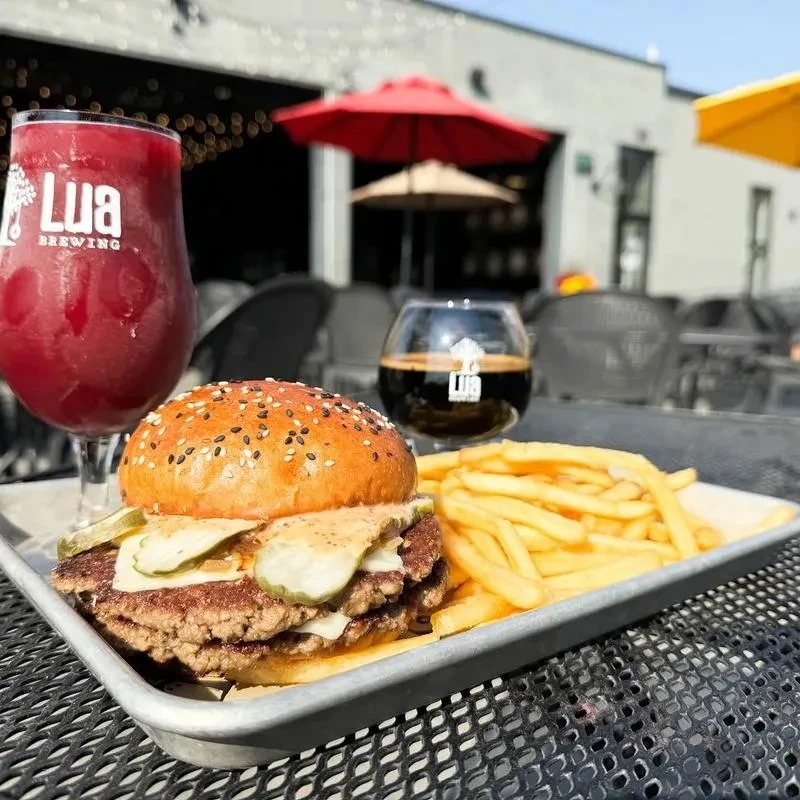 Double cheeseburger, fries, and two Lua Brewing beers on a patio.