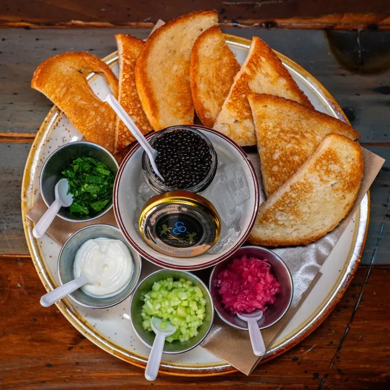 Caviar service platter with black caviar, accompaniments, and blini.