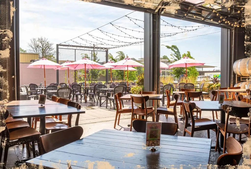 Expansive empty restaurant patio with pink umbrellas, string lights, and greenery.
