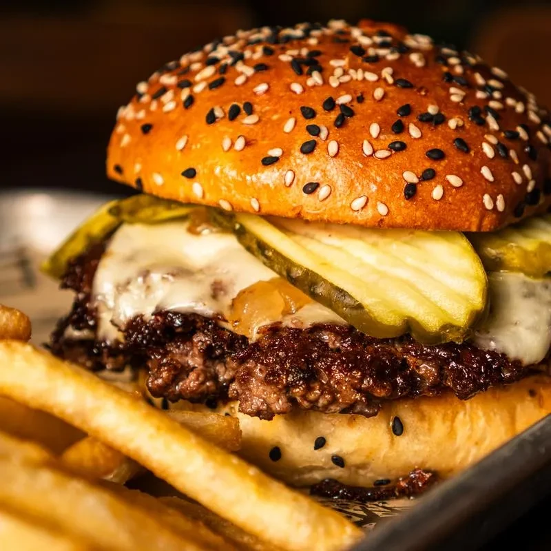 Gourmet beef burger with melted cheese, caramelized onions, pickles, and fries.