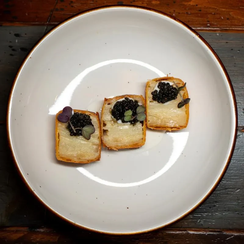 Three rectangular canapés with cream, black caviar, and microgreens.