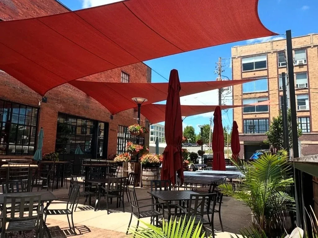 Outdoor dining patio with red awnings and brick buildings.