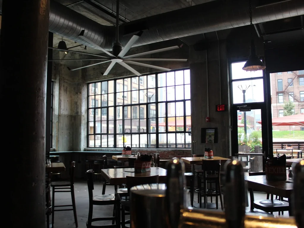 Empty industrial restaurant interior with exposed ducts and large windows.