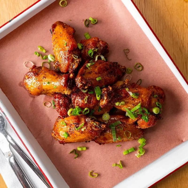 Crispy, sauced chicken wings garnished with green onions in a tray.