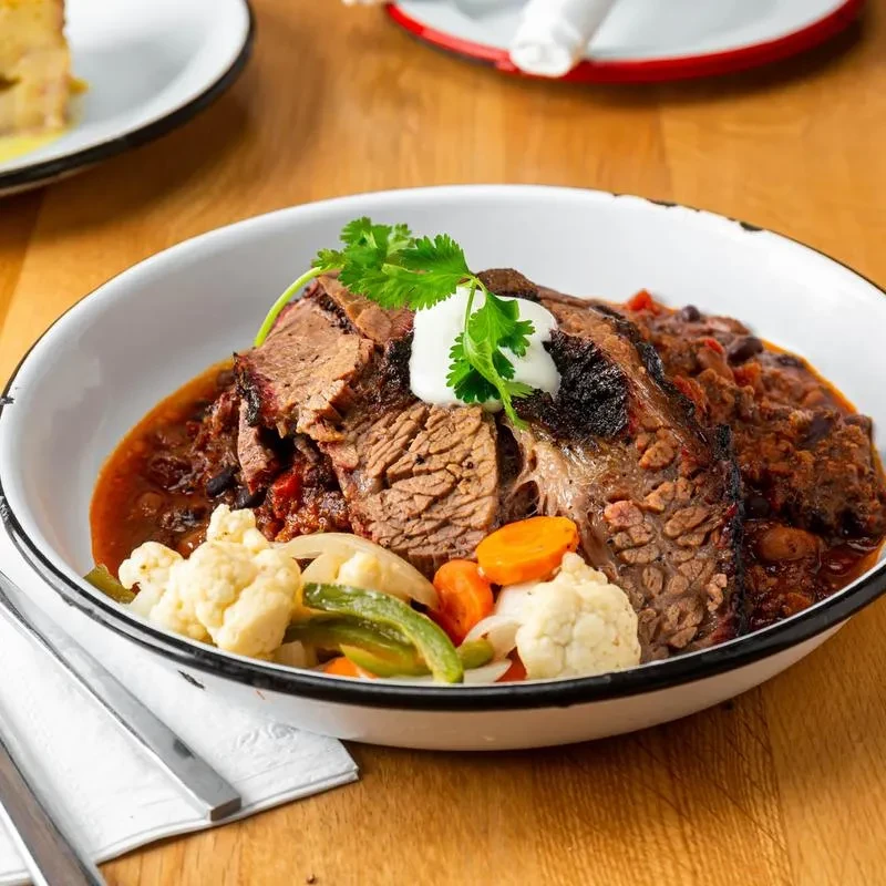 Braised meat, dark sauce, vegetables, cream, cilantro in rustic bowl.