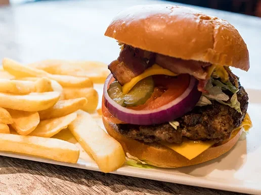 Gourmet burger with bacon, cheese, vegetables, and thick-cut fries.
