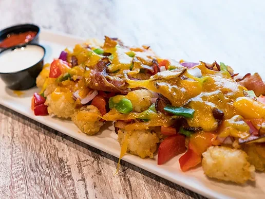 Loaded tater tots topped with melted cheese, bacon, peppers, and sauces.