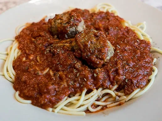 Overhead plate of spaghetti and two meatballs in tomato sauce with herbs.