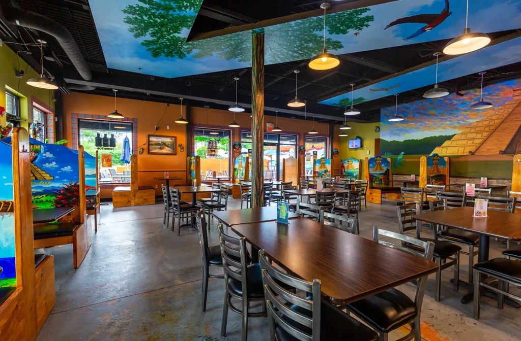 Vibrant, empty restaurant interior featuring tropical and Mayan-themed murals.