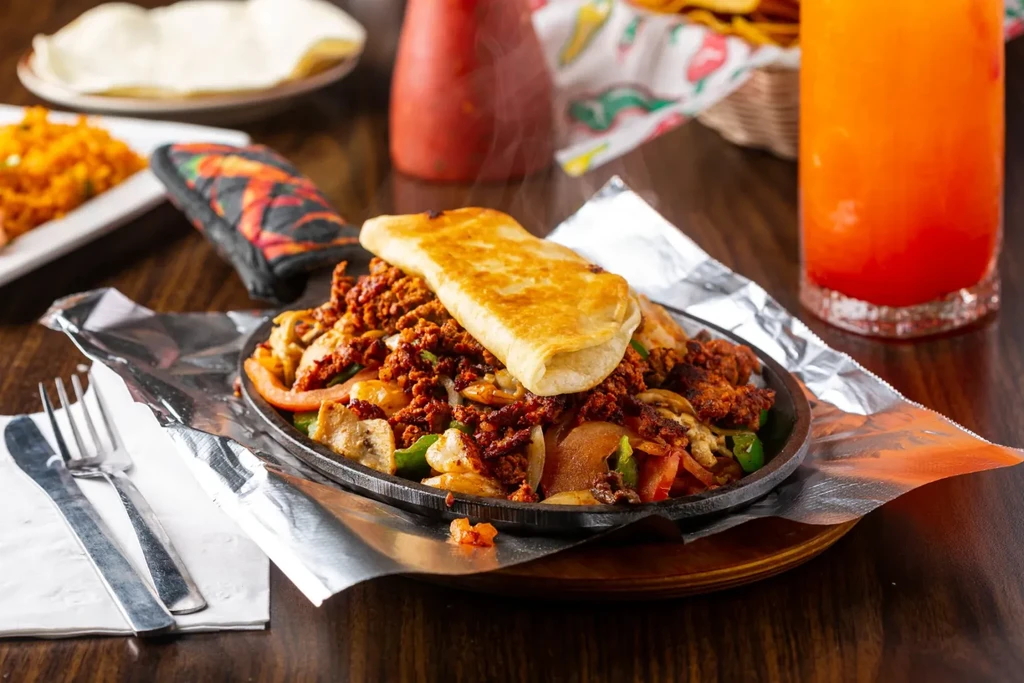 Sizzling fajitas with meat and vegetables in a cast-iron skillet.