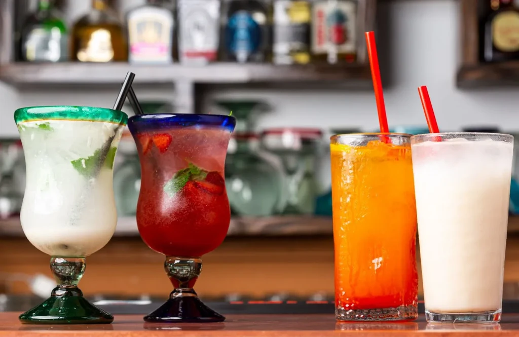 Four vibrant mixed drinks arranged on a polished wooden bar.