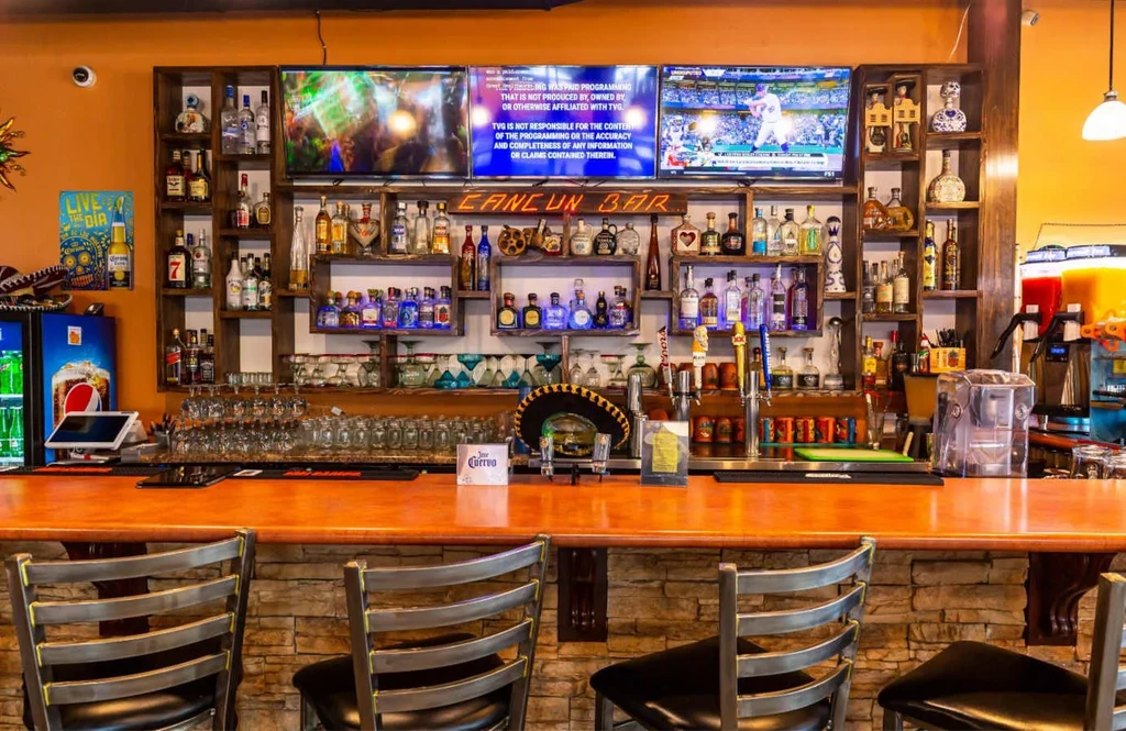 Vibrant Cancun Bar interior with extensive liquor display and televisions.