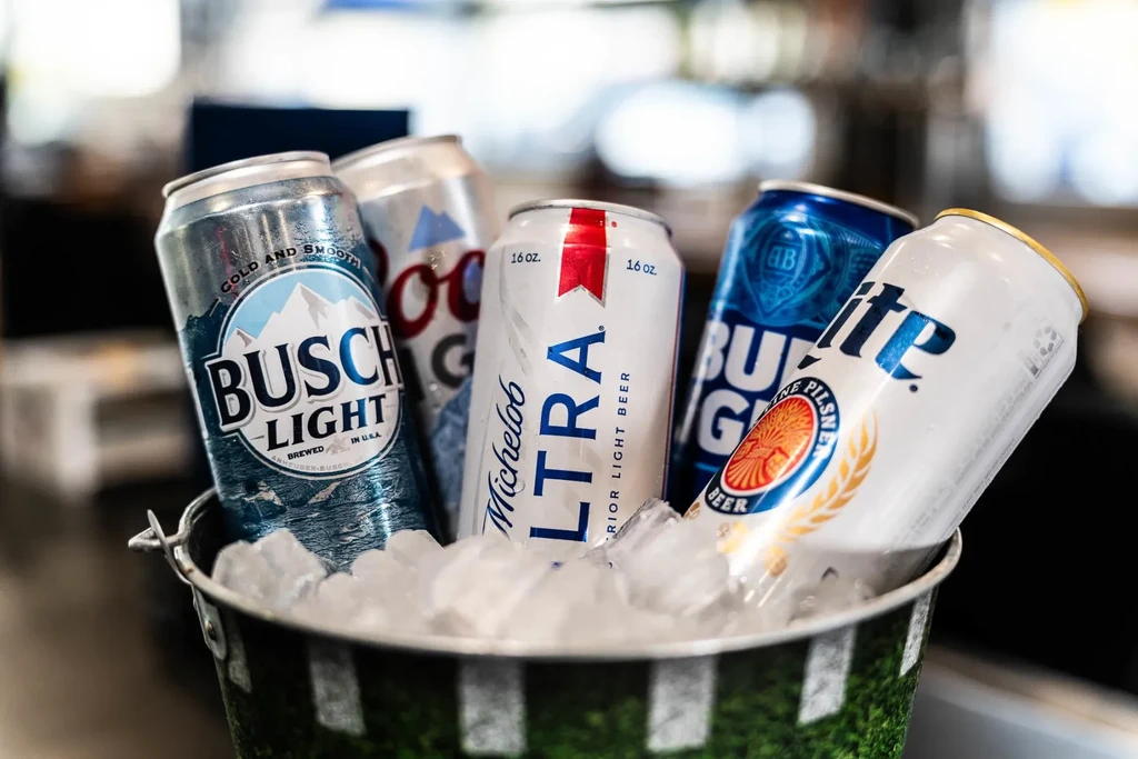Assorted cold beer cans with condensation in a green turf-like ice bucket.