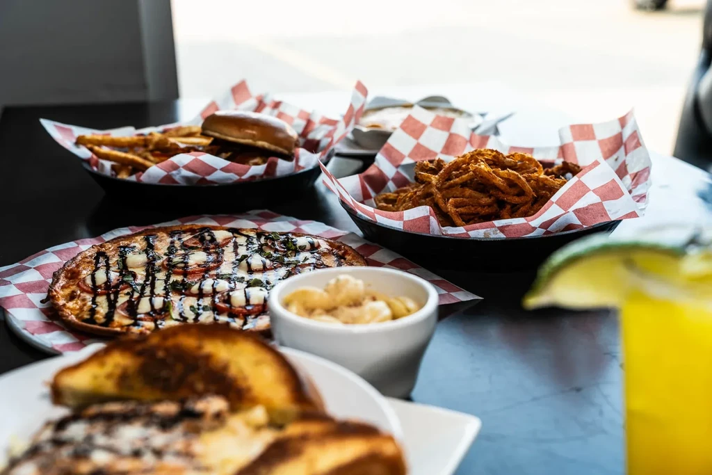 Table with pizza, burgers, fries, fried items, and a yellow drink.