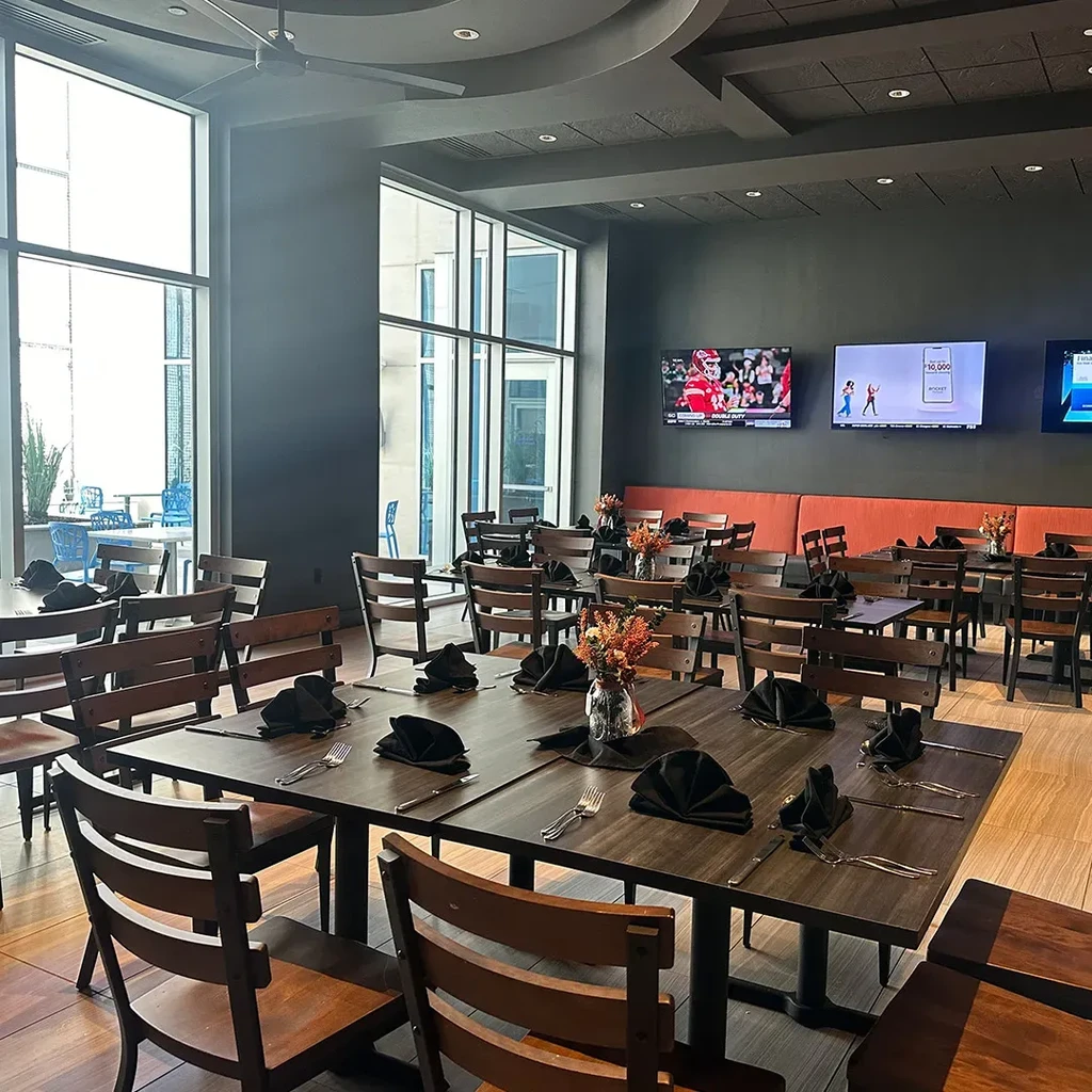 Empty modern restaurant interior with wooden tables, orange booth, and mounted TVs.