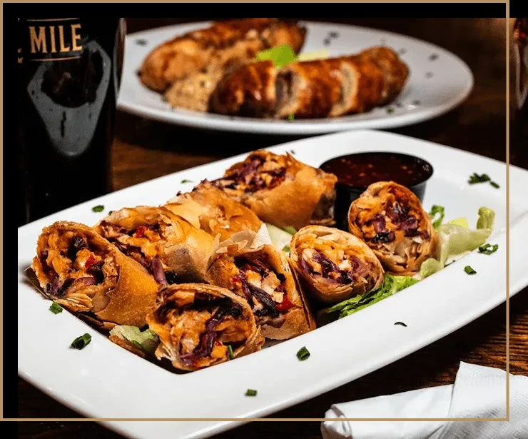 Golden-brown spring rolls, cut revealing colorful filling, with dipping sauce.