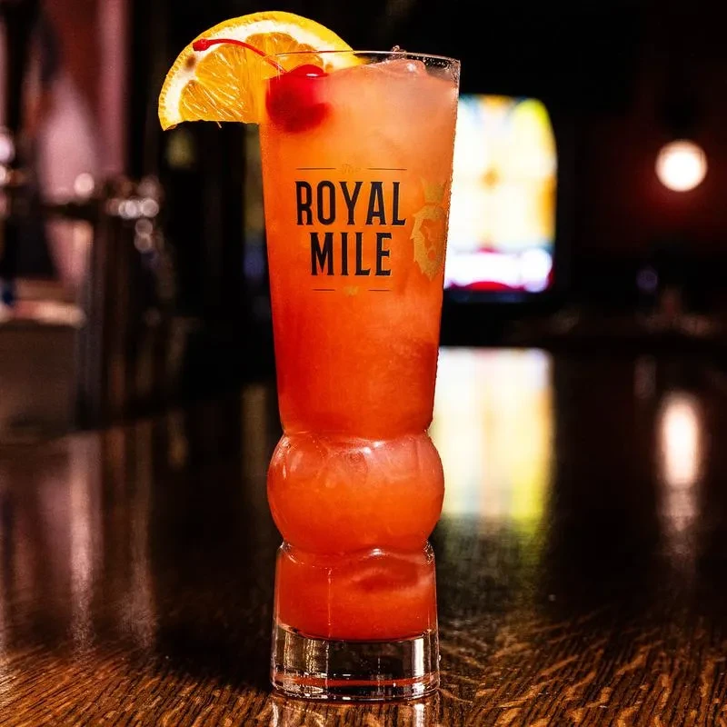Gradient cocktail with 'ROYAL MILE' on glass, garnished with orange and cherry.