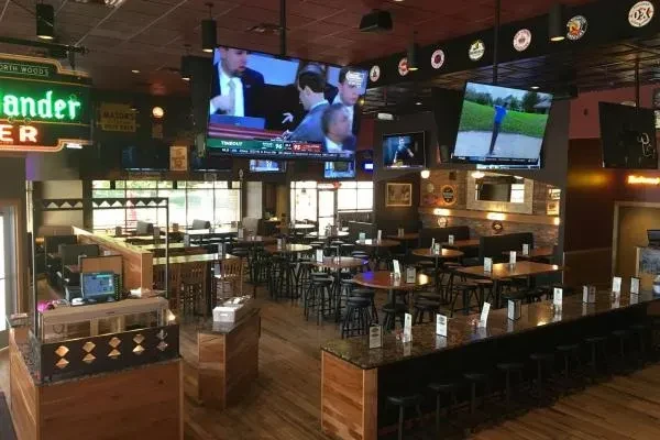 Empty casual sports bar interior with many TVs, various seating, warm decor.