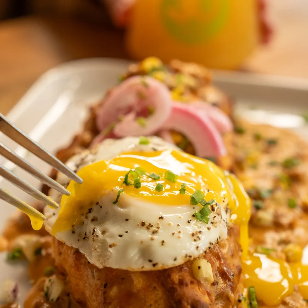Fried egg with runny yolk over biscuit and gravy, fork piercing yolk.