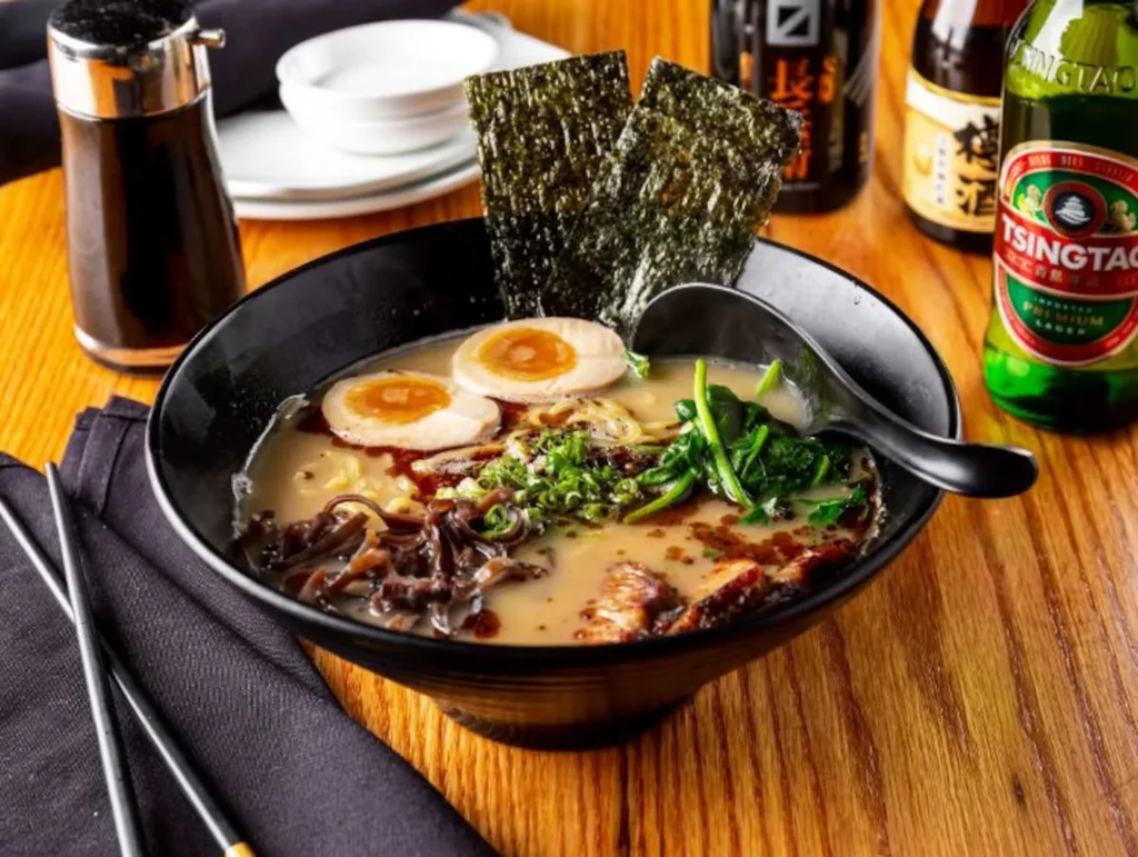 Close-up of ramen in a black bowl with eggs, meat, and nori.