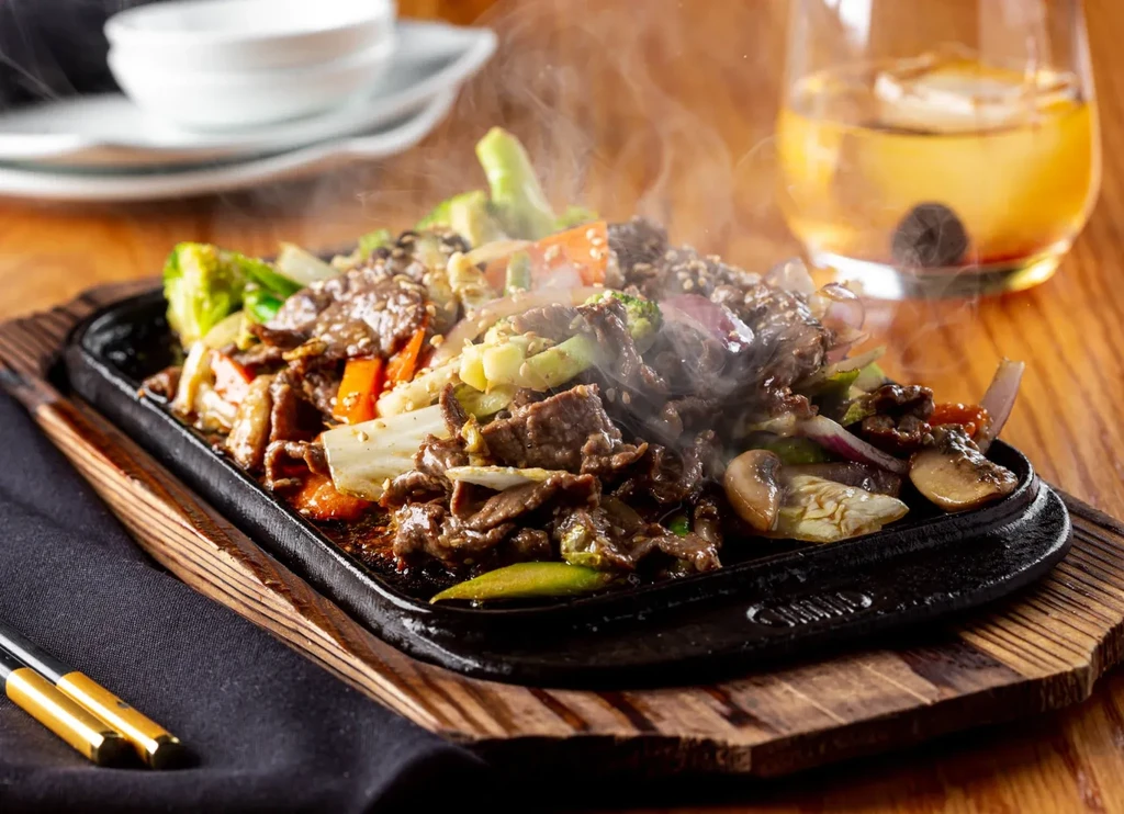 Sizzling stir-fried beef and vegetables on a cast iron platter.