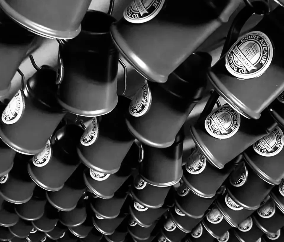 Rows of Court Avenue Brewing Co. mugs hanging upside down.
