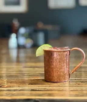 Copper mug with iced beverage and lime on rustic wood table.