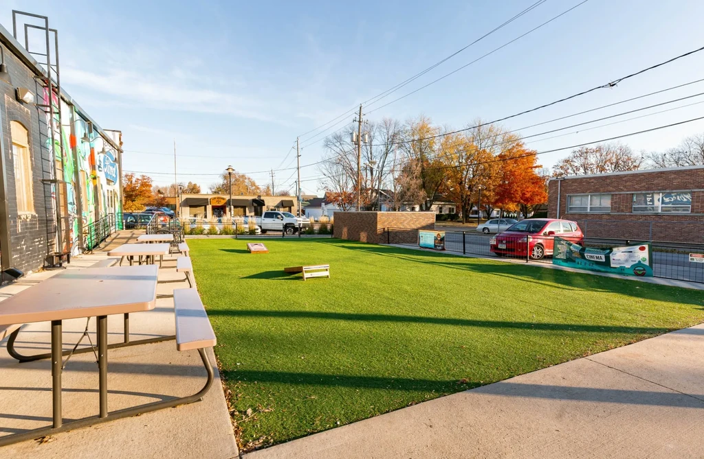 Outdoor patio with picnic tables, artificial turf, Ford mural, autumn trees.