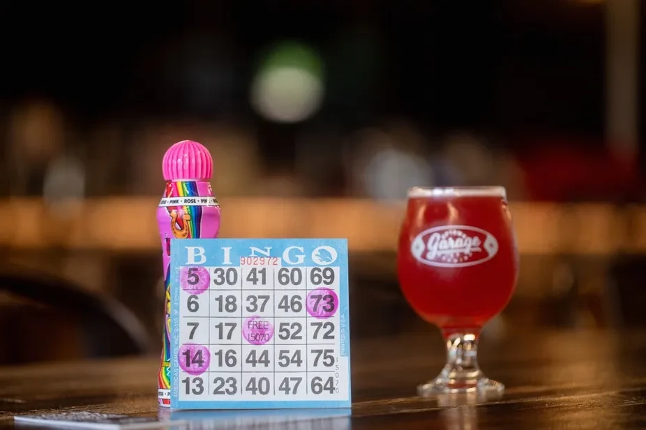 Bingo card, pink dauber, and beer in a 'Garage' glass on wood.