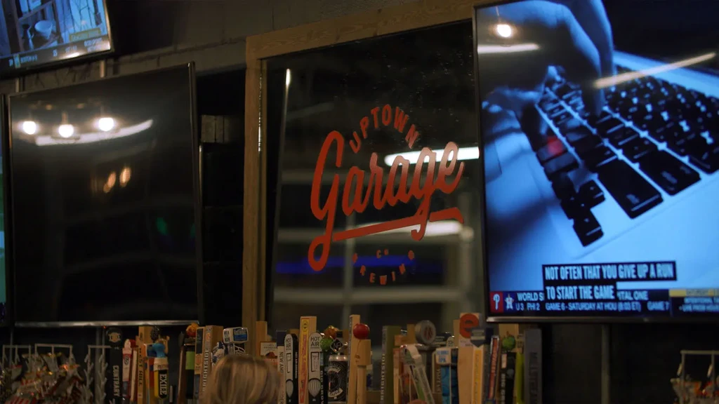 Multiple TVs, brewery logo mirror, and beer taps in a dim bar.