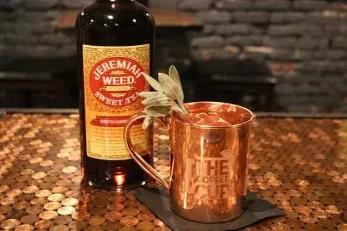 Jeremiah Weed liqueur bottle and copper mug on a penny bar.