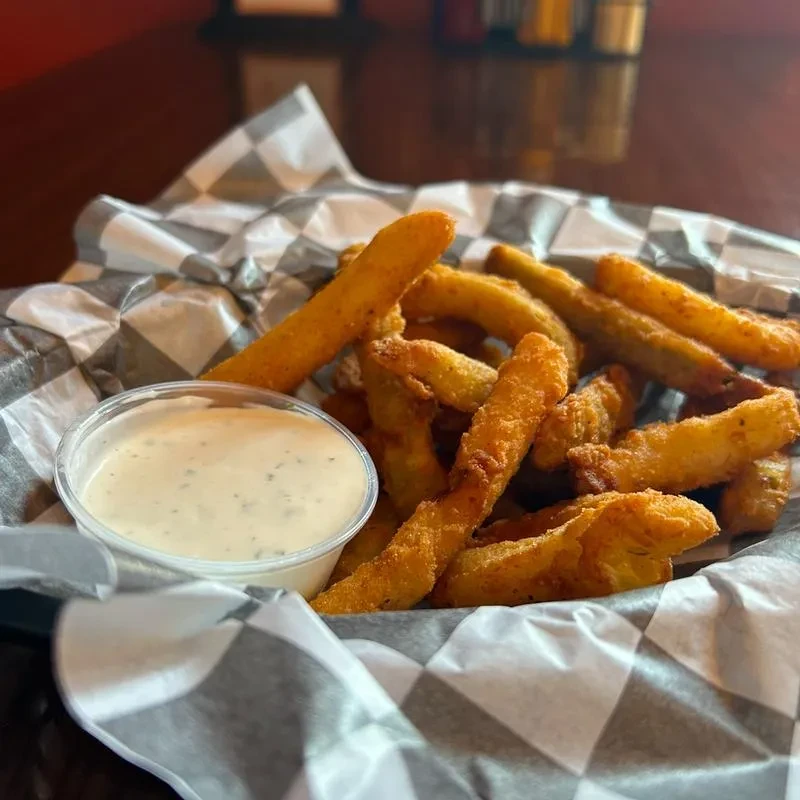 Basket of crispy golden fried pickles or zucchini sticks with creamy dip.