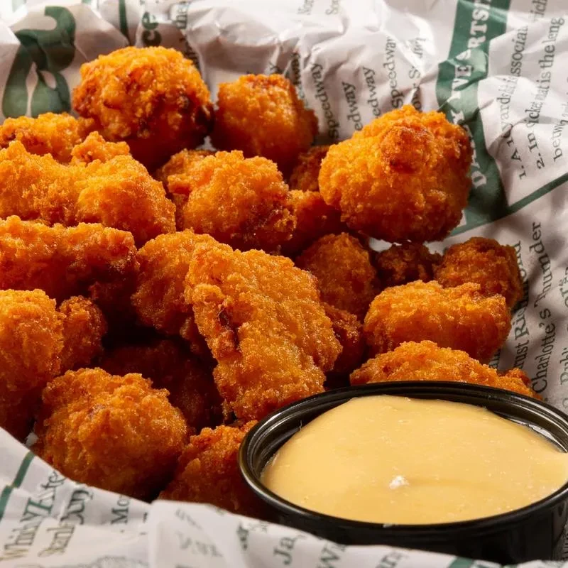 Golden-brown fried chicken pieces with dipping sauce in a paper-lined basket.