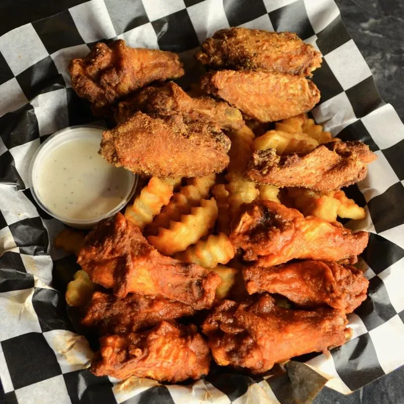 Chicken wings, crinkle-cut fries, dipping sauce in checkered basket.
