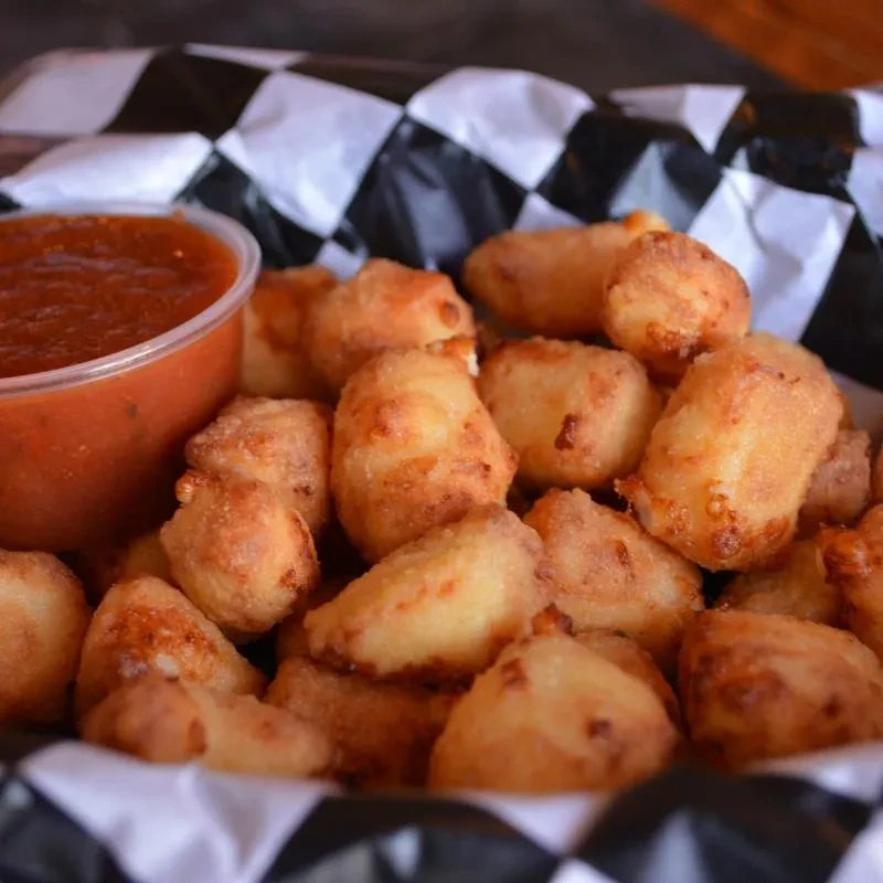 Golden fried cheese curds in checkered paper with marinara sauce.