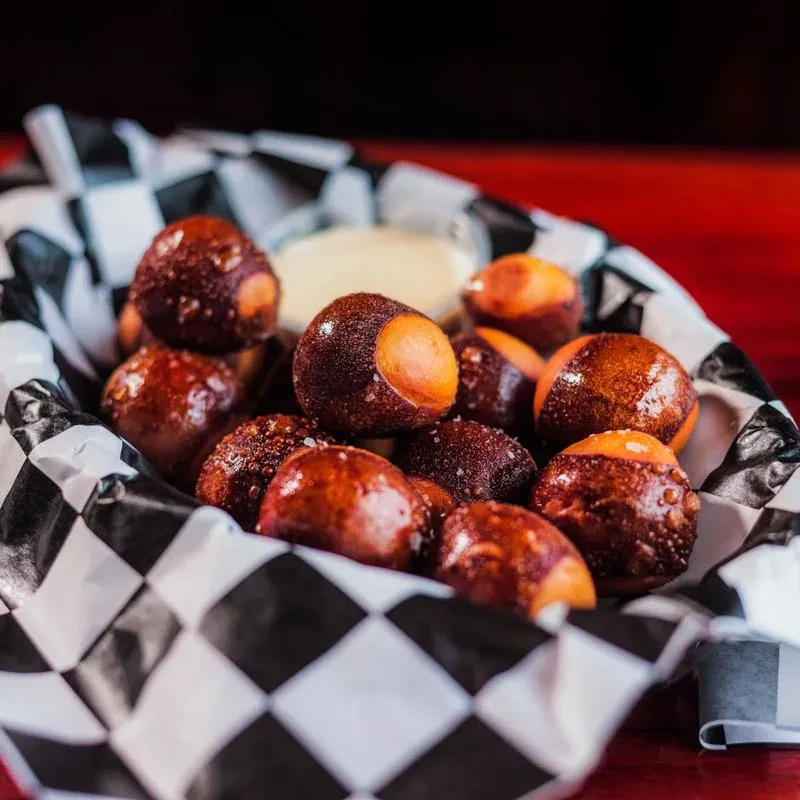 Close-up: Salted pretzel bites in checkered basket with dipping sauce.