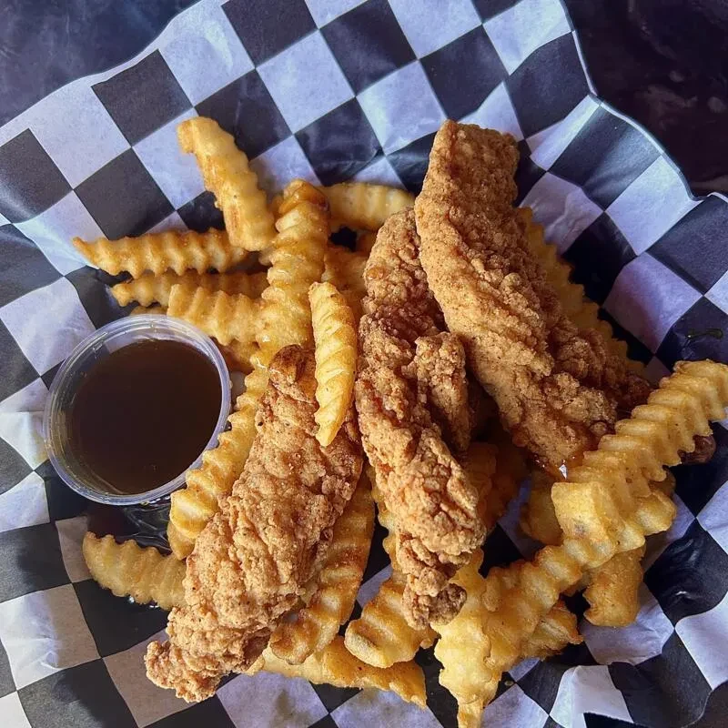 Golden chicken tenders, crinkle fries, and sauce in a checkered basket.