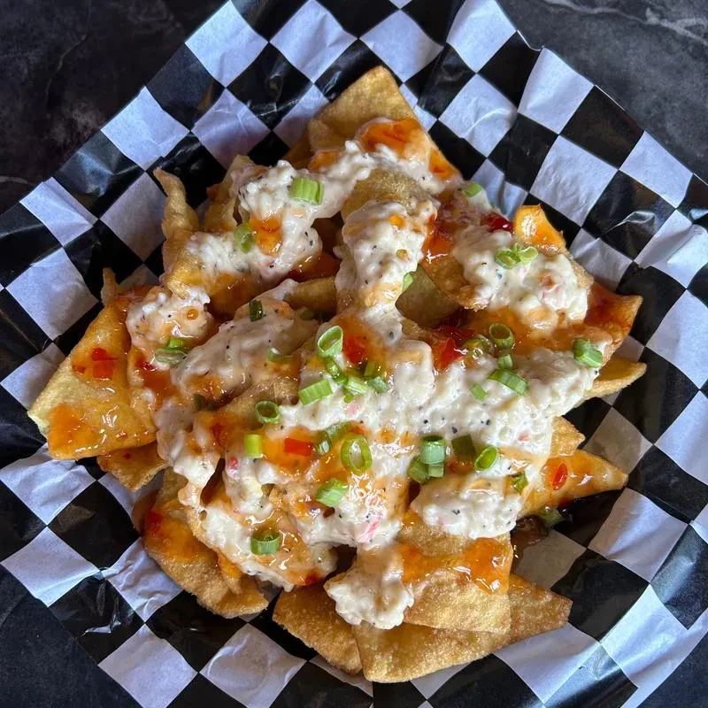 Close-up of crab rangoon nachos with sweet chili sauce and green onions.