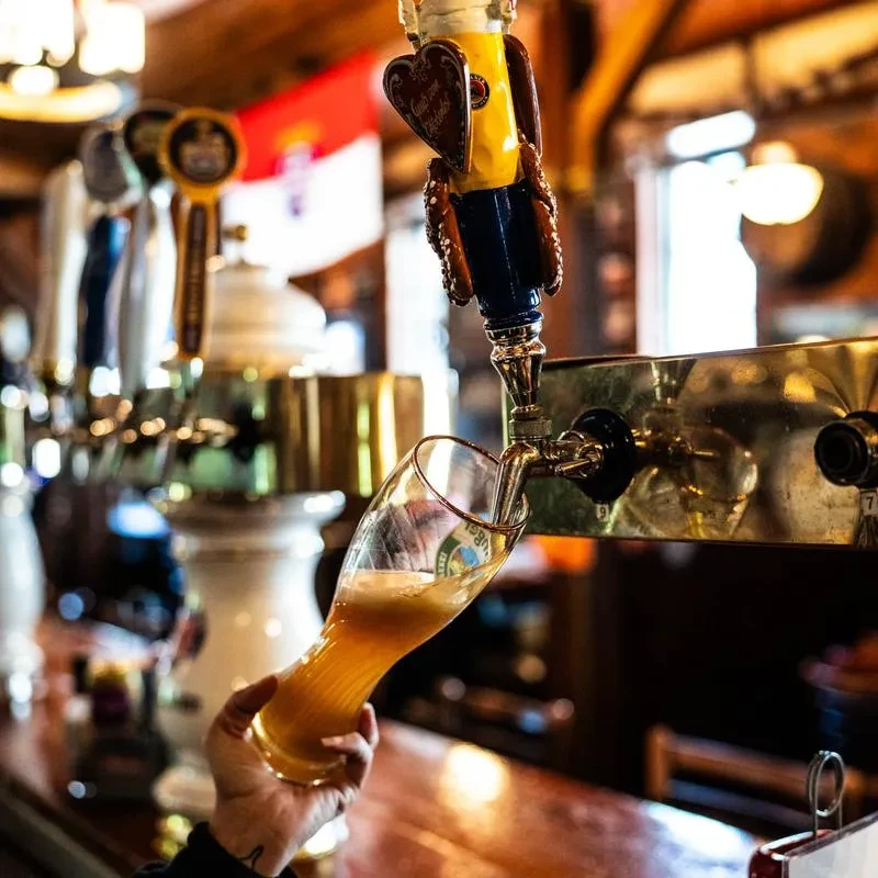 Hand holds a glass of golden beer pouring from a tap.