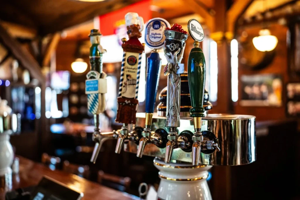Five distinct beer tap handles with various brand logos at a bar.