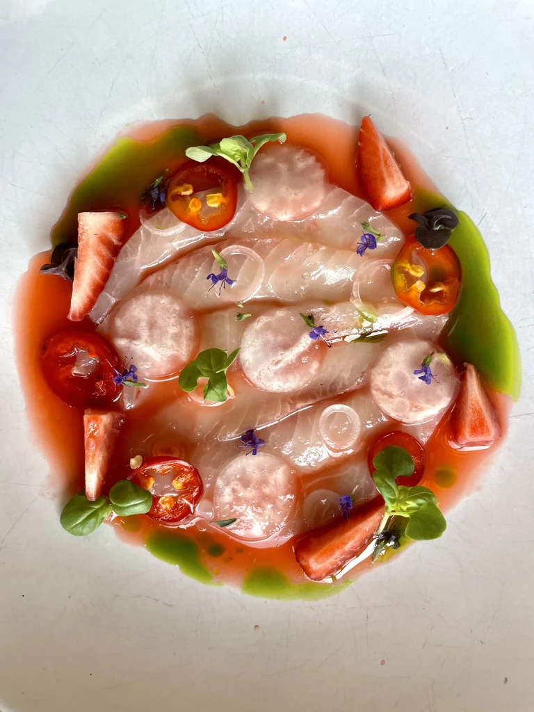Thin fish slices in pink sauce with tomatoes, strawberries, and flowers.