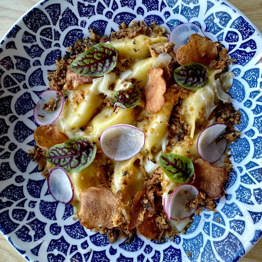 Plated pasta with creamy sauce, radish, microgreens, and crumbs.
