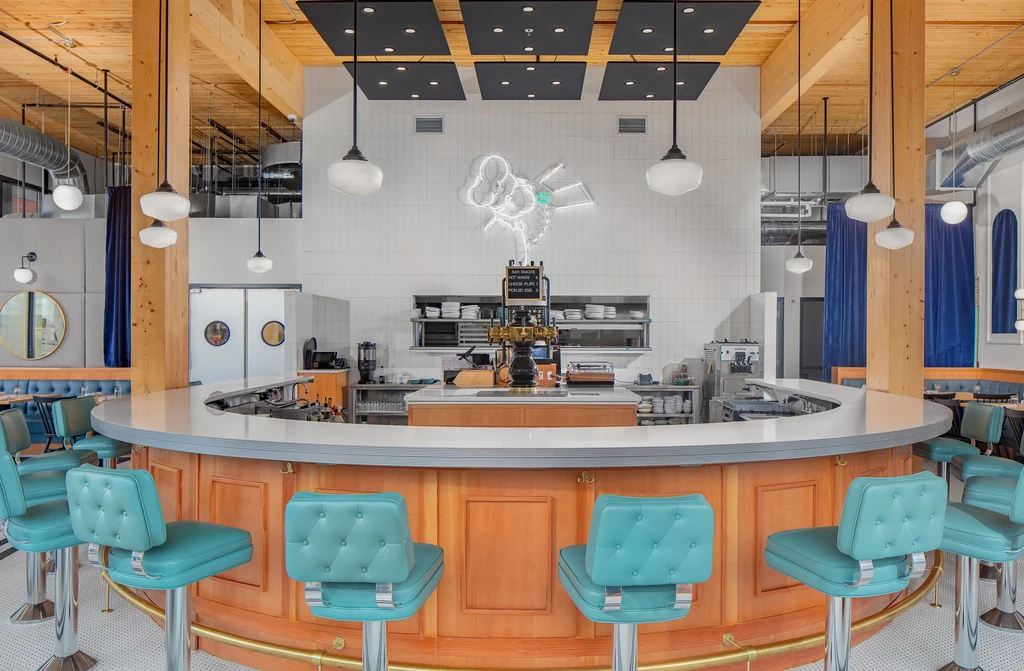 Modern industrial-chic restaurant interior with a large bar and neon sign.
