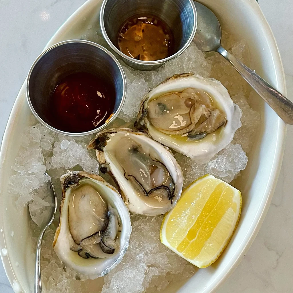 Three oysters on half shell with lemon, sauces, ice.